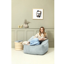 Vrouw zit ontspannen op een lichtblauwe corduroy zitzak in een modern ingerichte woonkamer met groene wandpanelen.