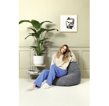 Een persoon zit in een grijze corduroy zitzak in een lichte woonkamer. Naast de zitzak staat een grote kamerplant in een witte pot.