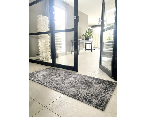 Vloerloper met vintage patroon in grijs op tegelvloer in een lichte kamer met glazen deur.