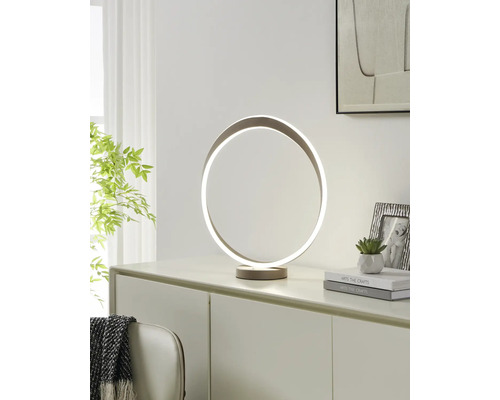 Moderne LED-tafellamp in de vorm van een ring op een dressoir. Lichte kamer met een plant, boeken en een fotolijst.