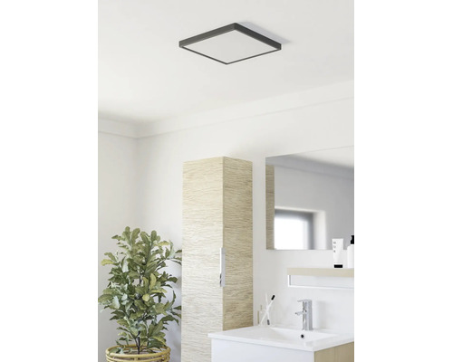 Moderne badkamer met een vierkante plafondlamp, een slanke kolomkast met houtlook, een witte wastafel en een kamerplant.