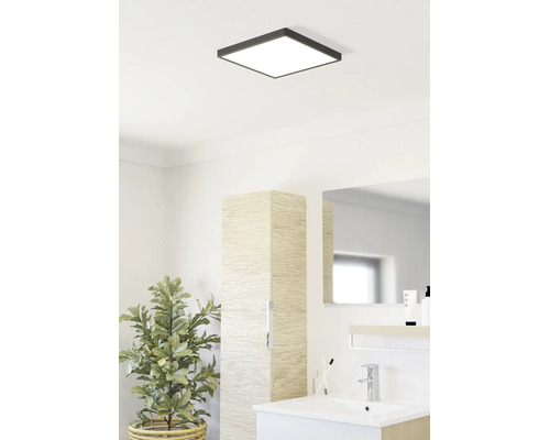 Lichte badkamer met vierkante LED-plafondlamp, modern wastafelmeubel, hoge kast met houtlook en kamerplant.