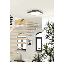 Vierkante plafondlamp in een lichte, moderne ruimte met een houten trap en glazen balustrade.