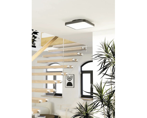 Vierkante plafondlamp in een lichte, moderne ruimte met een houten trap en glazen balustrade.