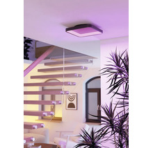 Moderne vierkante plafondlamp met ledverlichting in een lichte woonruimte met zwevende trap, glazen leuning en kamerplanten.