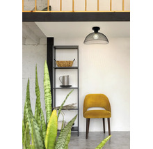 Moderne plafondlamp van zwart draadgaas in een lichte kamer met een metalen rek en gele gestoffeerde stoel.