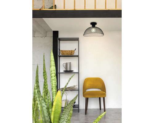 Moderne plafondlamp van zwart draadgaas in een lichte kamer met een metalen rek en gele gestoffeerde stoel.