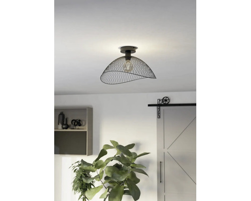 Industriële plafondlamp met een zwarte metalen gaaskap en zichtbare lichtbron in een moderne kamer met plant en schuifdeur.