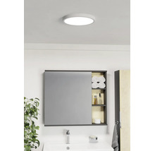 Lichte badkamer met ronde plafondlamp, spiegelkast met open planken voor handdoeken en verzorgingsproducten en een witte wastafel.
