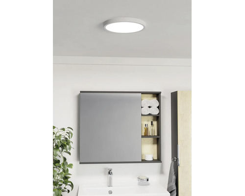 Lichte badkamer met ronde plafondlamp, spiegelkast met open planken voor handdoeken en verzorgingsproducten en een witte wastafel.
