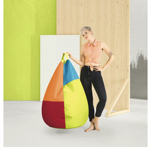 Een vrouw staat naast een grote, druppelvormige, veelkleurige zitzak met handvat in een moderne studio-omgeving met houten elementen.