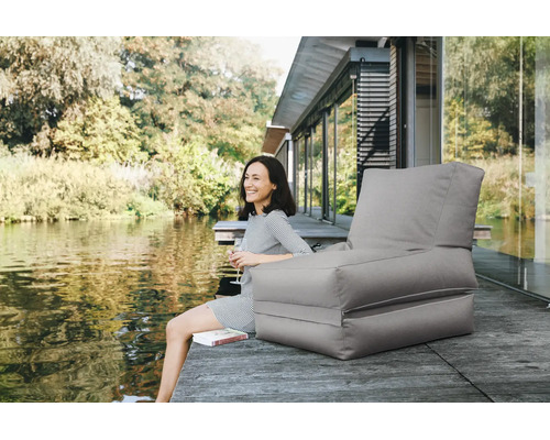 Grijze outdoor zitzak in de vorm van een fauteuil op een houten steiger aan een meer. Tuinloungemeubilair voor buiten.