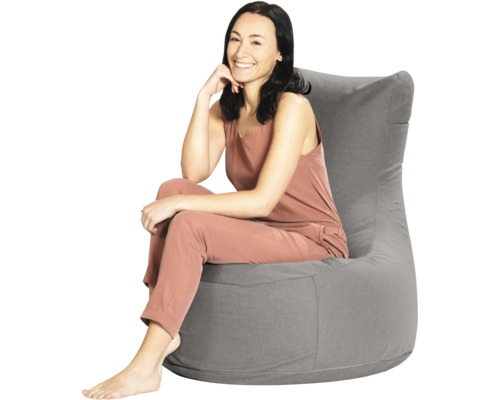 Een vrouw zit in een grijze zitzak met een hoge rugleuning van textiel.