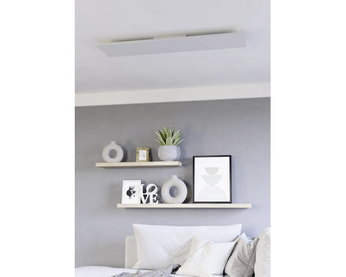 Plat LED-paneel als plafondlamp in een modern ingerichte woonkamer boven wandplanken met decoratie.