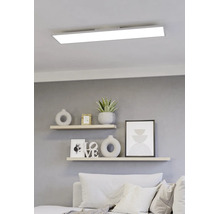 Modern, rechthoekig LED-paneel aan een wit plafond boven een lichte woonkamer met wandplanken en decoratieve elementen.