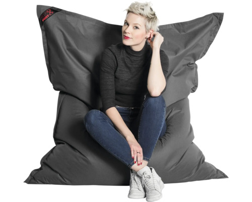 Een vrouw zit op een grote, antracietkleurige Big Foot zitzak van slijtvast materiaal.