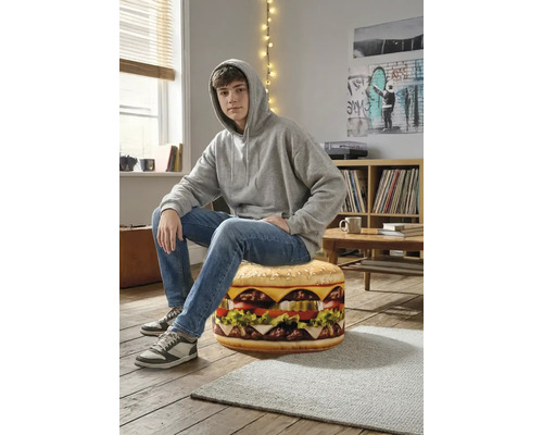 Een tiener zit op een ronde zitzak in de vorm van een hamburger in een lichte kamer met houten vloer.