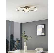 Moderne LED-plafondlamp met vier overlappende lichtringen in een lichte kamer met grijze muren, een tafel met vaas en uitzicht op de stad.