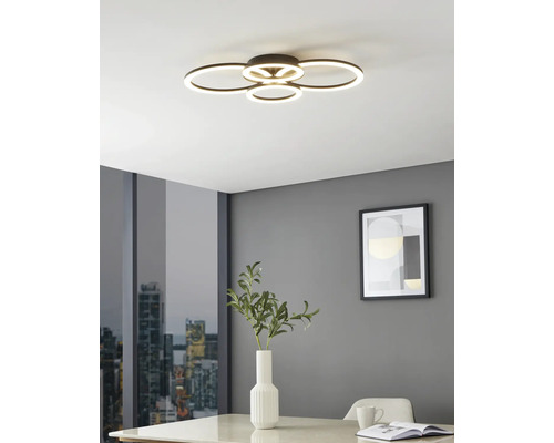 Moderne LED-plafondlamp met vier overlappende lichtringen in een lichte kamer met grijze muren, een tafel met vaas en uitzicht op de stad.