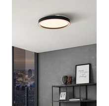 Platte, ronde zwarte LED-plafondlamp aan een wit plafond in een modern interieur met grijze wand en metalen rek.