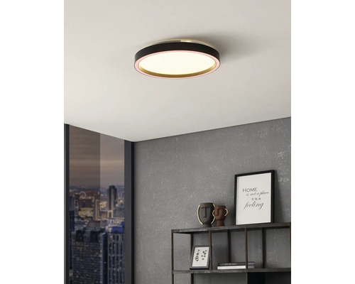 Ronde LED-plafondlamp met zwarte behuizing in een modern ingerichte kamer met grijze muur en raam met stadszicht.