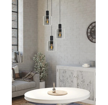 Driepunts hanglamp met glazen kappen in een lichte woonkamer met een witte bakstenen muur, bank en salontafel in industriële stijl.