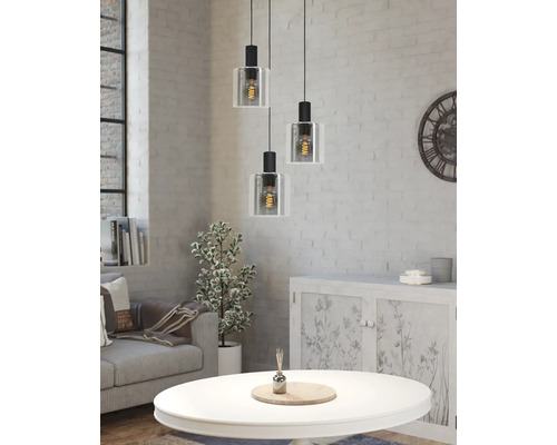 Driepunts hanglamp met glazen kappen in een lichte woonkamer met een witte bakstenen muur, bank en salontafel in industriële stijl.