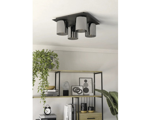 Moderne 4-lichts plafondlamp met cilindrische kappen boven een rek met decoratie en planten.