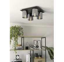 Vierlichts plafondlamp met zwarte metalen basis en cilindrische kappen van rookglas in een lichte woonkamer met een open kast.