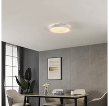 Ronde LED-plafondlamp in moderne eetkamer met wandpanelen in steenlook, eettafel en beklede stoelen. De lamp heeft een verlichte rand.