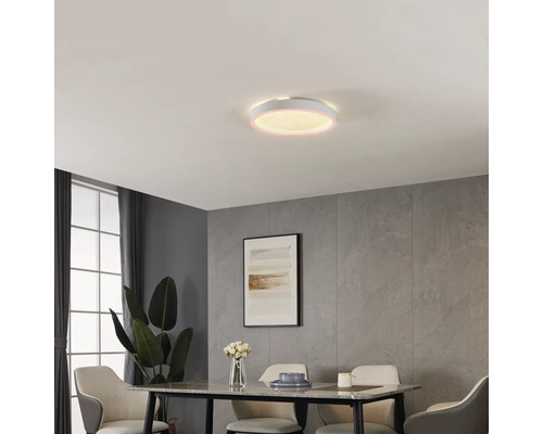 Ronde LED-plafondlamp in moderne eetkamer met wandpanelen in steenlook, eettafel en beklede stoelen. De lamp heeft een verlichte rand.