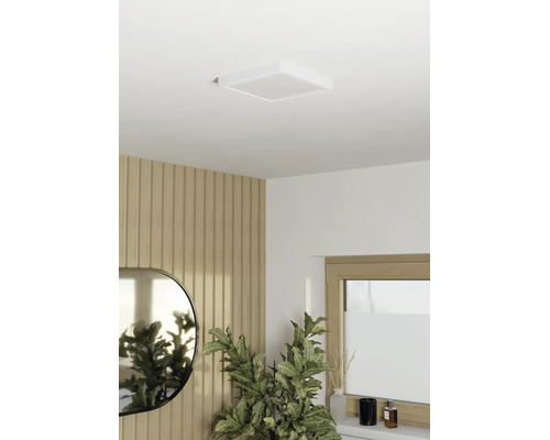 Vierkante LED-plafondlamp aan wit plafond in moderne kamer met houten wandpanelen, spiegel en groene plant.