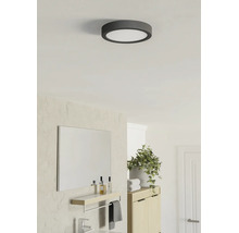 Ronde LED-plafondlamp in een lichte, moderne badkamer met spiegel, houten kast en kamerplant.