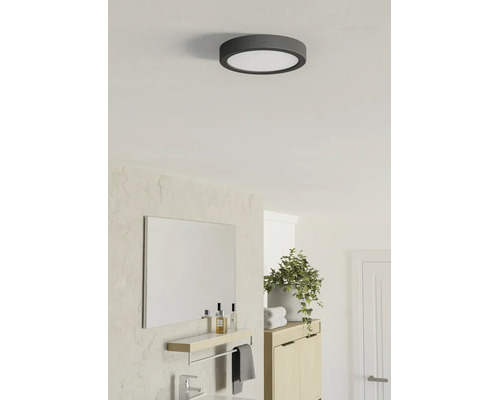 Ronde LED-plafondlamp in een lichte, moderne badkamer met spiegel, houten kast en kamerplant.