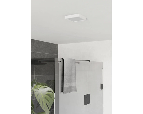 Moderne badkamer met vierkante plafondlamp, glazen douchewand met zwart beslag, grijze handdoek en donkere wandtegels.
