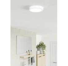 Ronde led-plafondlamp in een lichte, moderne badkamer boven een spiegel met planchet en een kamerplant.