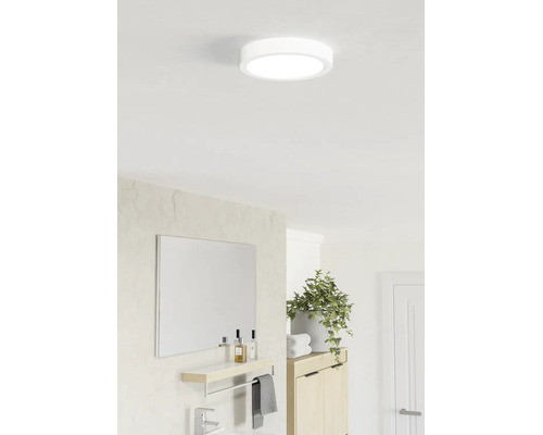 Ronde led-plafondlamp in een lichte, moderne badkamer boven een spiegel met planchet en een kamerplant.