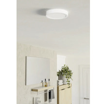 Ronde platte LED-plafondlamp in een lichte, modern ingerichte badkamer met spiegel, planchet en plant.