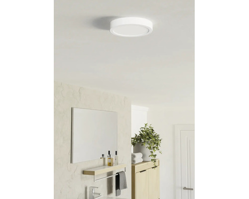 Ronde platte LED-plafondlamp in een lichte, modern ingerichte badkamer met spiegel, planchet en plant.