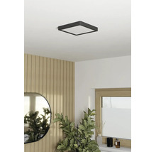 Vierkante led-plafondlamp in een lichte, modern ingerichte kamer met wandpanelen met houtlook, een ovale spiegel en een kamerplant.
