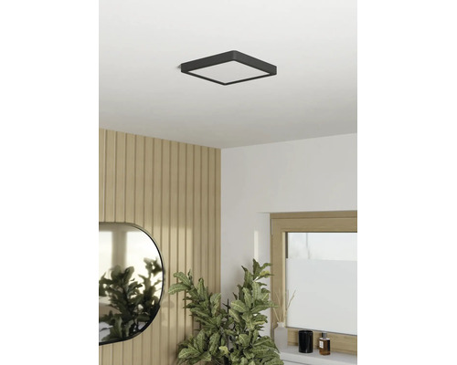 Vierkante led-plafondlamp in een lichte, modern ingerichte kamer met wandpanelen met houtlook, een ovale spiegel en een kamerplant.