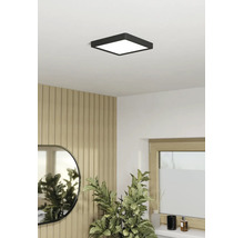 Vierkante, zwarte LED-plafondlamp in een lichte kamer met houten wandpanelen, spiegel en kamerplant.