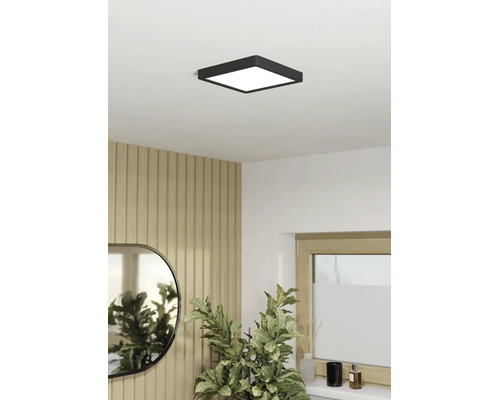 Vierkante, zwarte LED-plafondlamp in een lichte kamer met houten wandpanelen, spiegel en kamerplant.