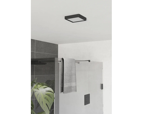 Moderne badkamer met een vierkante zwarte LED-plafondlamp, een glazen douchewand, grijze tegels en een groene kamerplant.