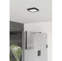 Vierkante, platte plafondlamp in het zwart in een moderne badkamer met glazen douchewand en grijze tegels.