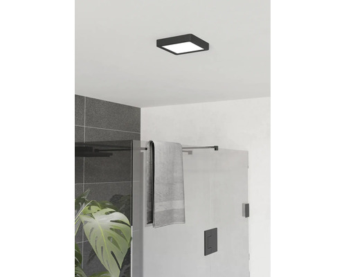 Vierkante, platte plafondlamp in het zwart in een moderne badkamer met glazen douchewand en grijze tegels.