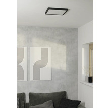 Vierkante plafondlamp met zwart frame in lichte, moderne woonkamer met grijze wand, bank en abstracte kunst.