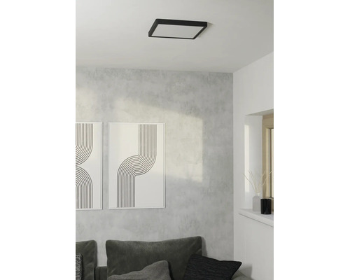 Vierkante plafondlamp met zwart frame in lichte, moderne woonkamer met grijze wand, bank en abstracte kunst.