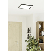 Vierkante plafondlamp met donker frame in een lichte woonkamer met houten deur, kast en kamerplant.