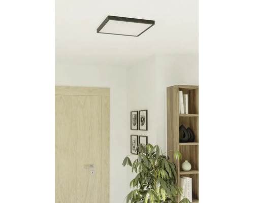 Vierkante LED-plafondlamp met donker frame in een lichte, moderne kamer met houten deur, boekenkast en kamerplant.